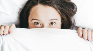 woman-peeking-out-from-under-bed-covers.jpg